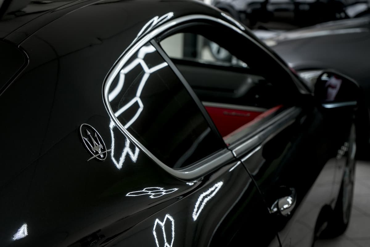 Tylny błotnik czarnego Maserati z ostrymi refleksami świateł na lakierze
